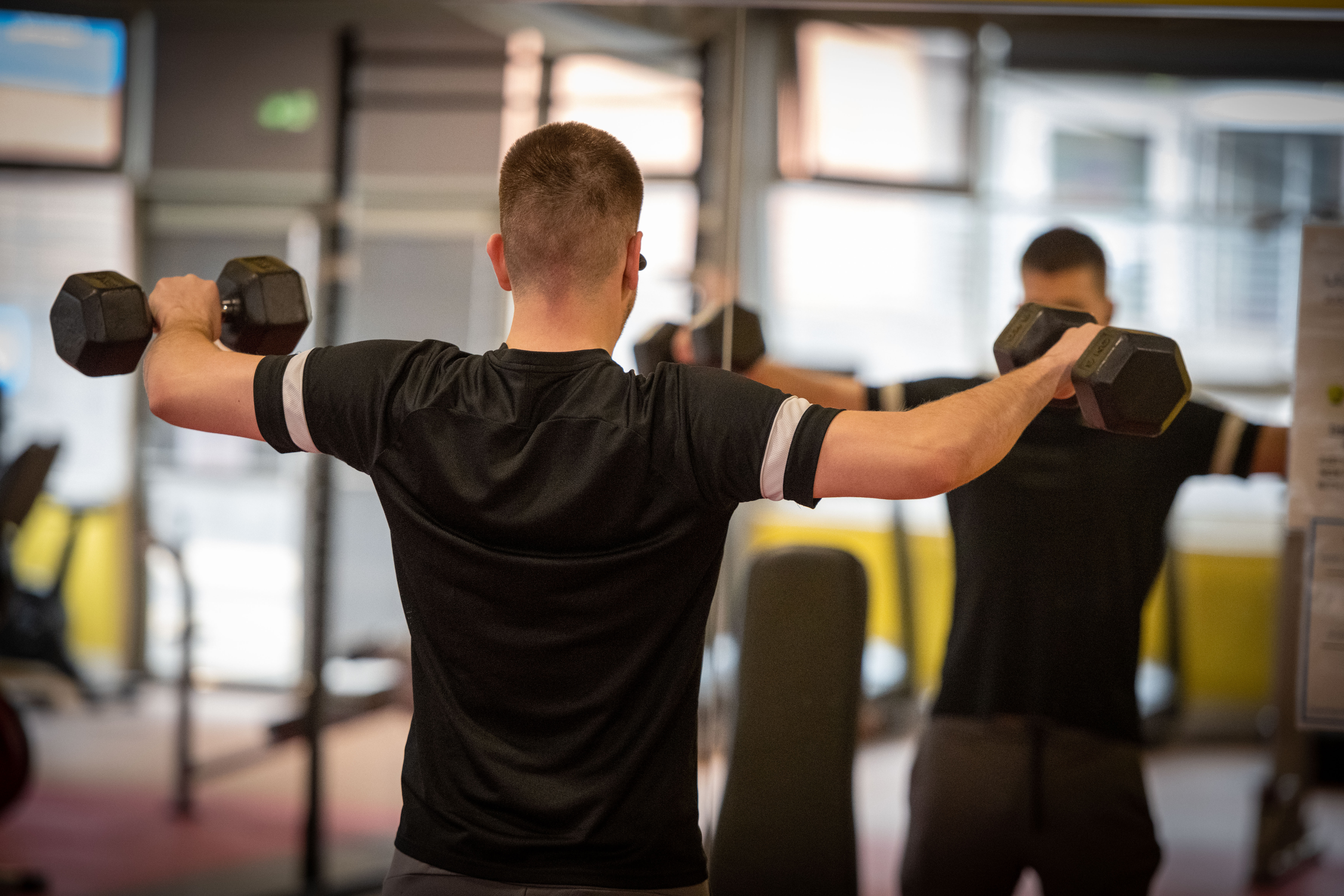 Man standing in front of a mirror using two dumbbells