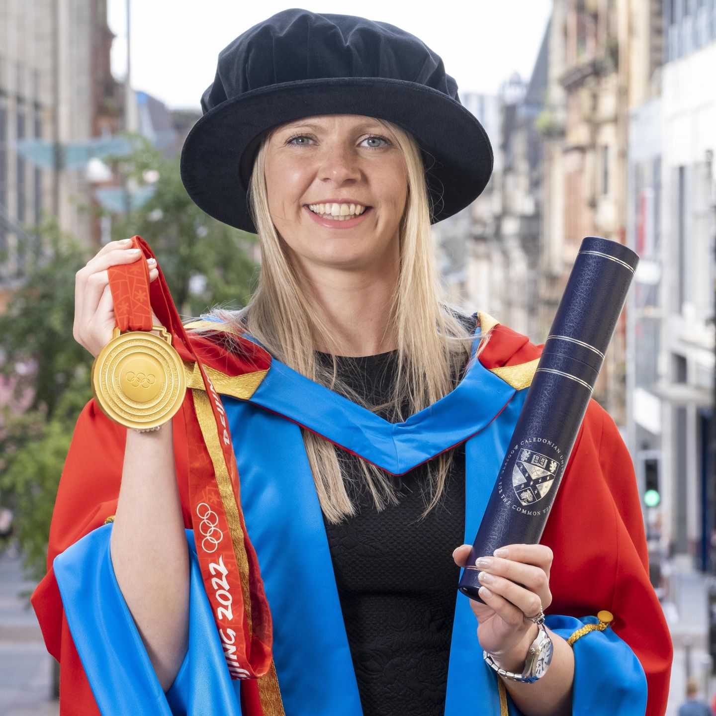 An image of Vicky Wright, a GCU alumna and a Scottish curler, holding her Olympic Gold medal in her graduation robes.