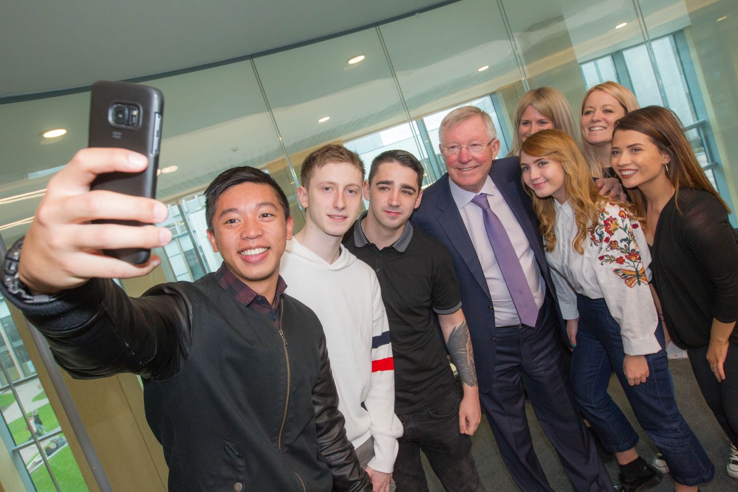 A group of Common Good Scholarship recipients with Sir Alex Ferguson and one of them is taking a selfie of the group.