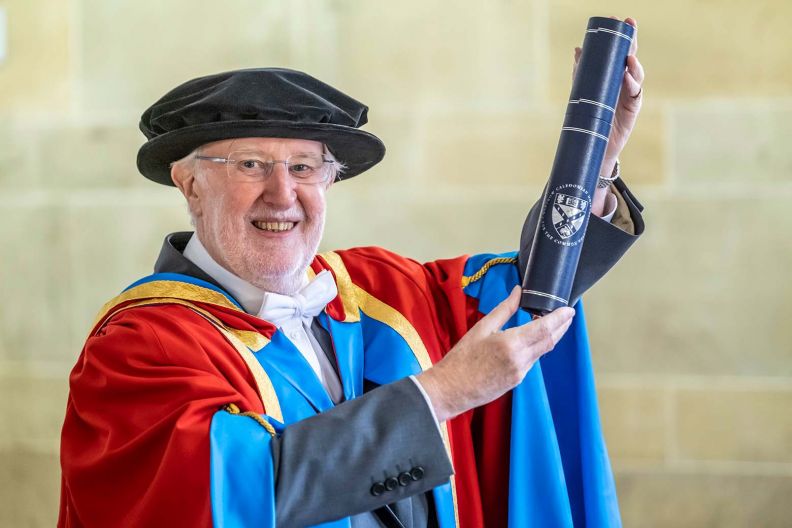 	GCU Honorary Graduate Dr Ian Young wearing his graduation hood and hat and holding a degree container .