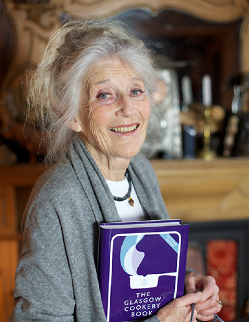 An image of Phyllida Law, GCU alumna, Honorary Graduate, actress and writer, holding a copy of the Glasgow Cookery Book.