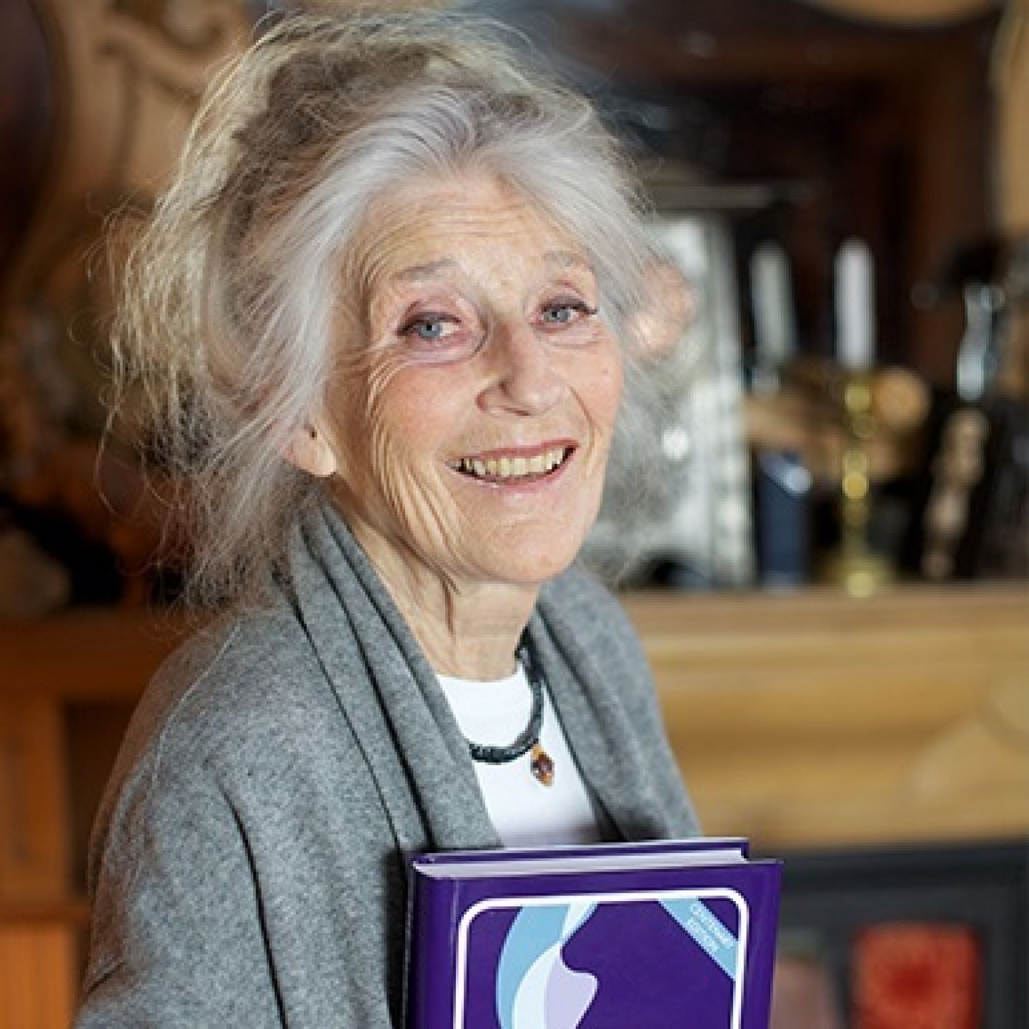 A square image of Phyllida Law, GCU alumna, Honorary Graduate, actress and writer, holding a copy of the Glasgow Cookery Book.