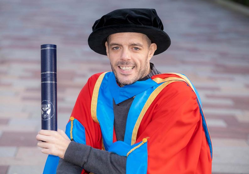 	GCU Honorary Graduate Dr Michael Kerr wearing his graduation hood and hat and holding a degree container.