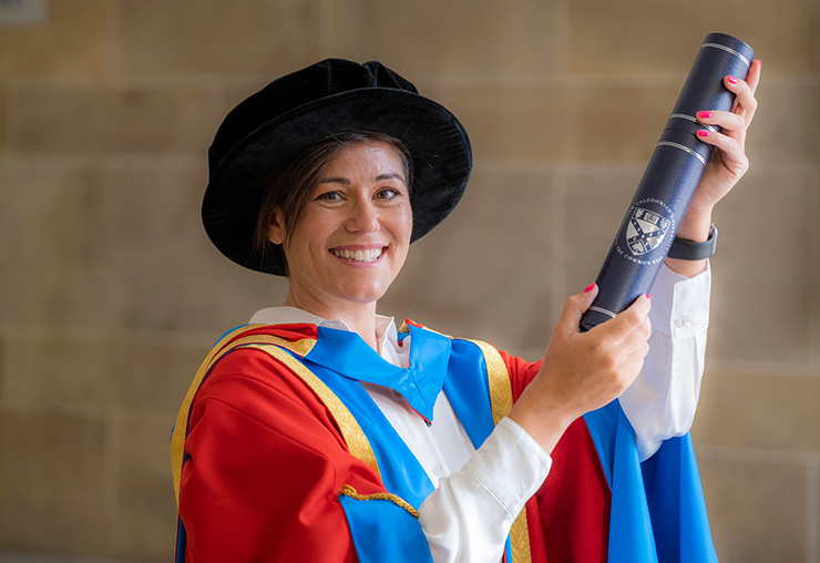 GCU Honorary Graduate Dr Eilidh Barbour wearing her graduation hood and hat and holding a degree container.