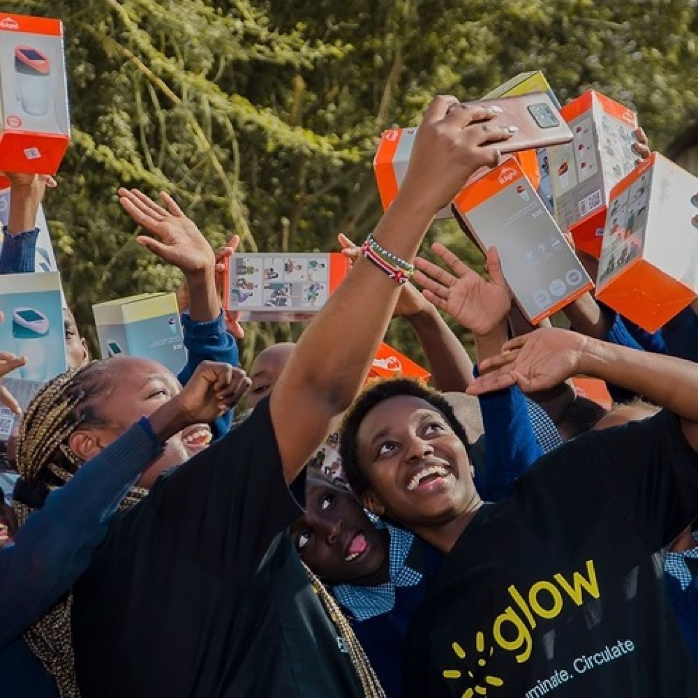 An image of ALC students and 2022 Magnusson winners Cynthia Gichuki and Reggie Okoko with children holding solar lamp boxes and taking a selfie.