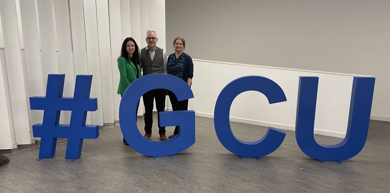 Three people standing behind large blue #GCU lettering stands