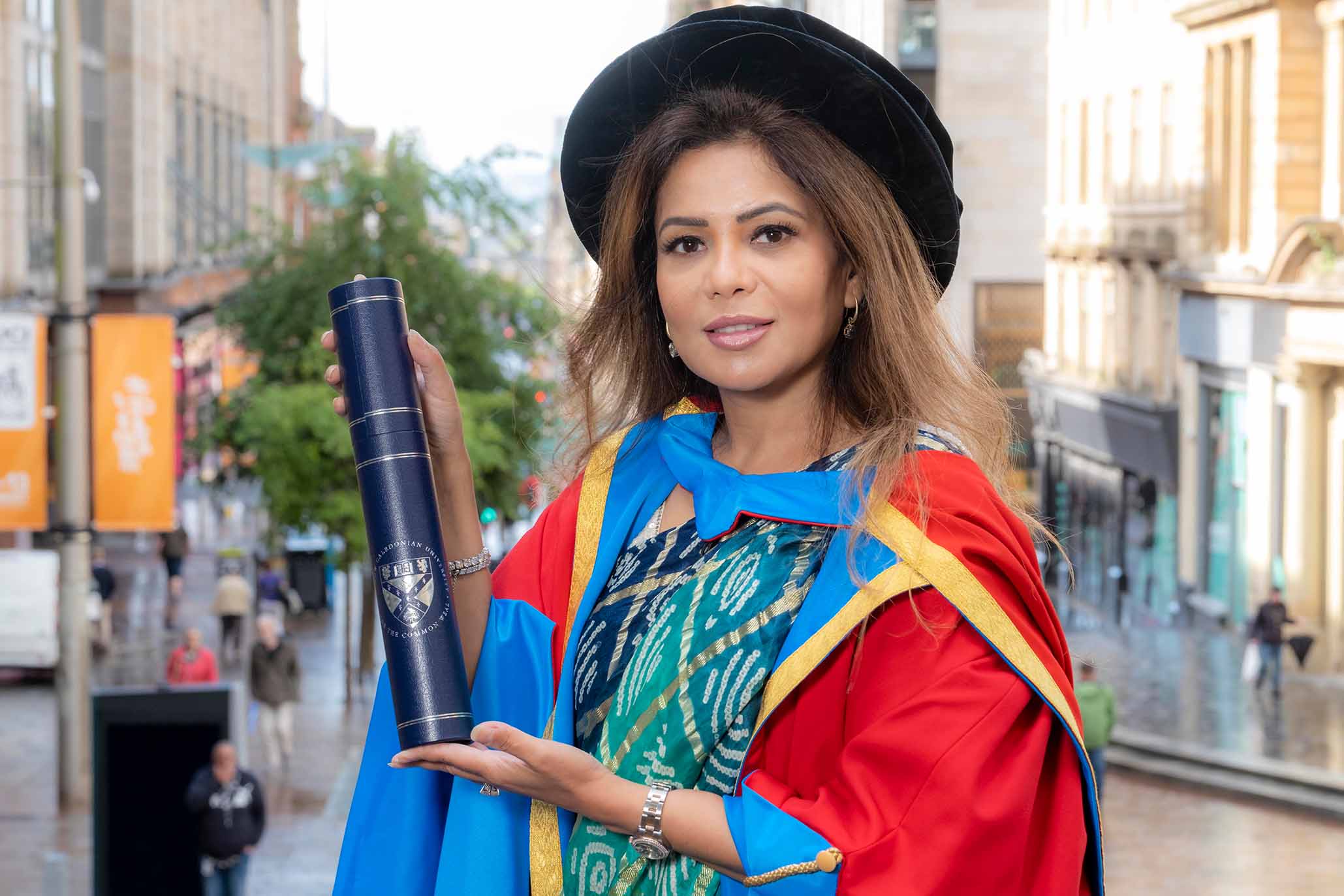 GCU Honorary Graduate Dr Poonam Gupta wearing her graduation hood and hat and holding a degree container.