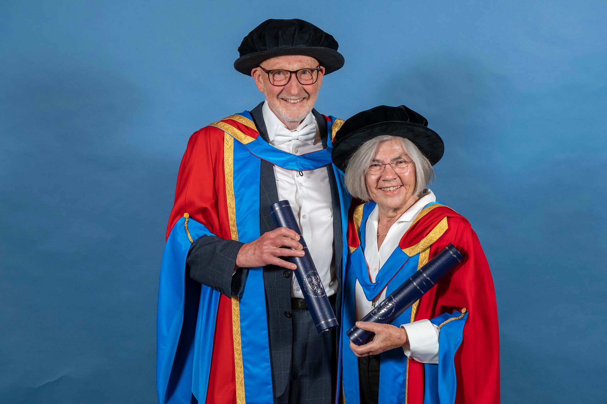 GCU Honorary Graduates Drs John and Senga Bond wearing their graduation hoods and hats and holding their degree containers.