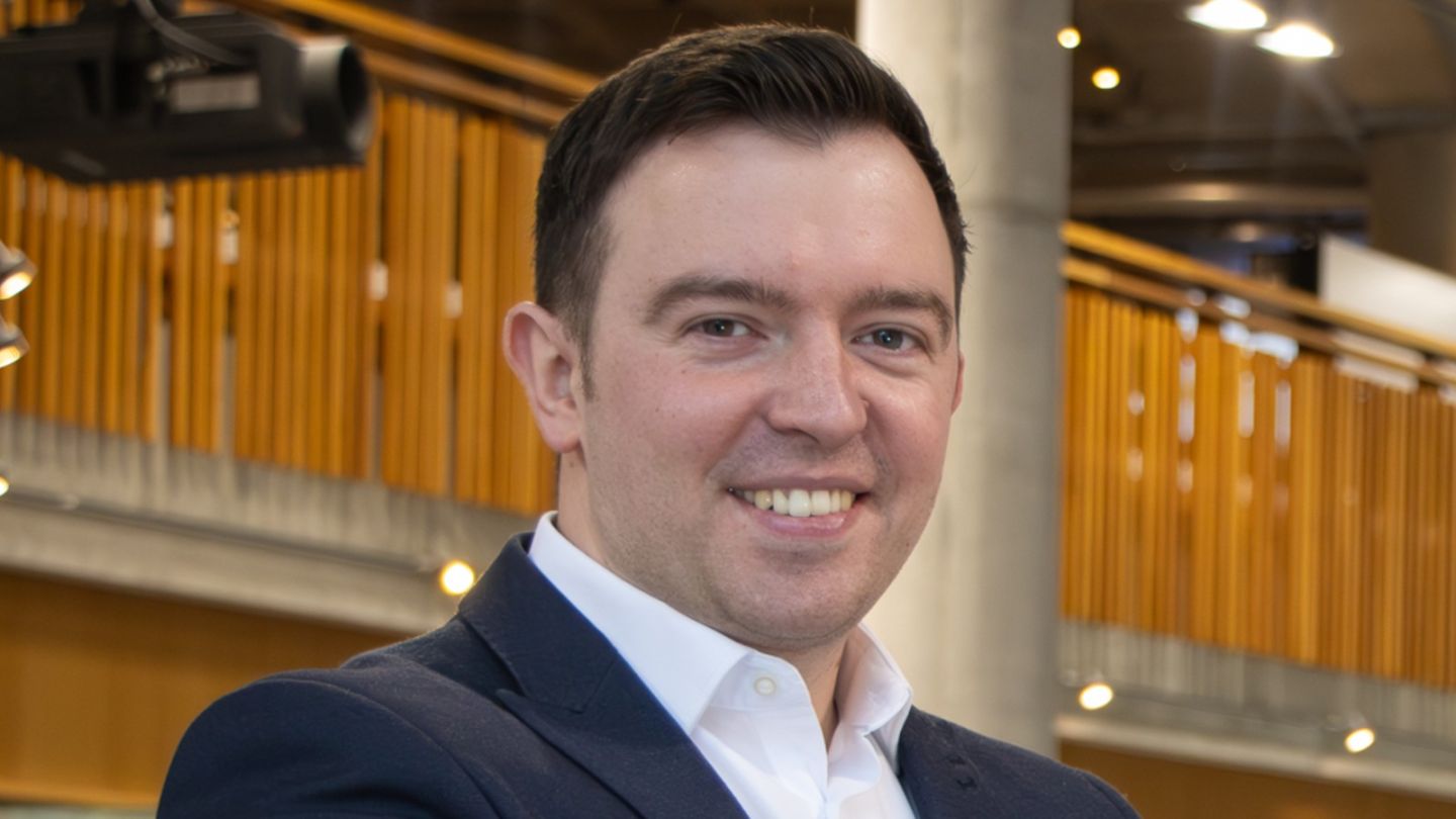 A photo of Jordan Reid smiling on the ground floor of the Sir Alex Ferguson Library