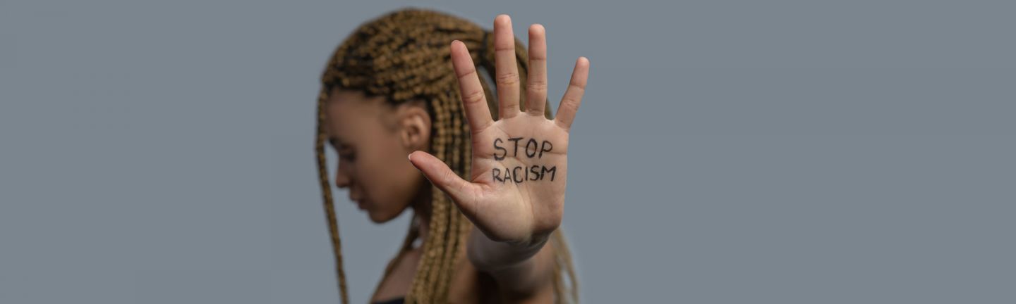 Person standing with head down and the words STOP RACISM written on their hands
