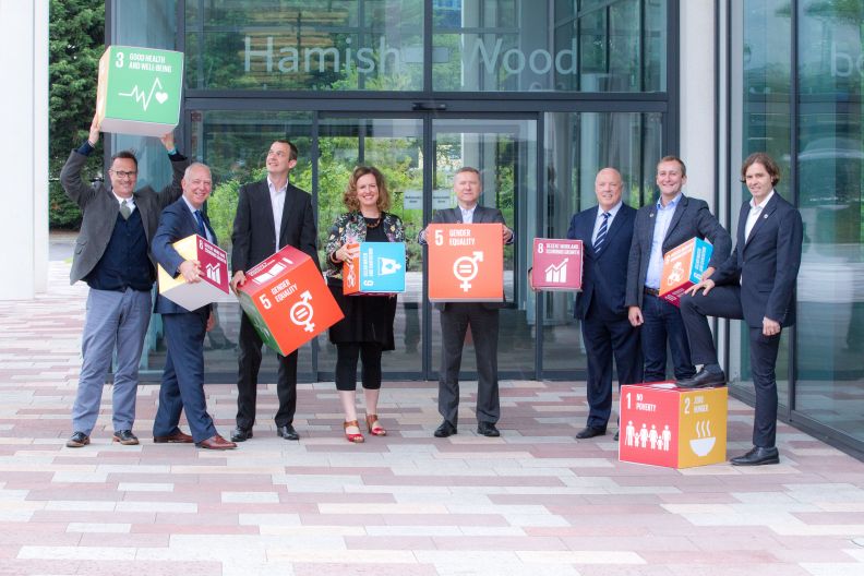 GCU staff holding SDG cubes, standing outside the Hamish Wood Building on Glasgow campus. Photo taken in June 2017.